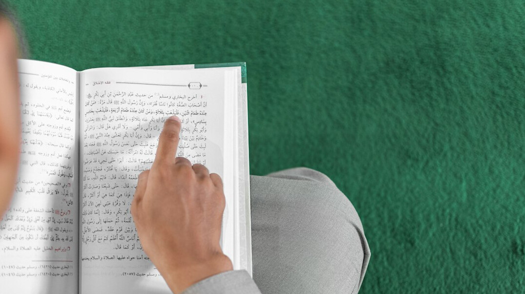 Hand writing notes in a notebook next to a laptop