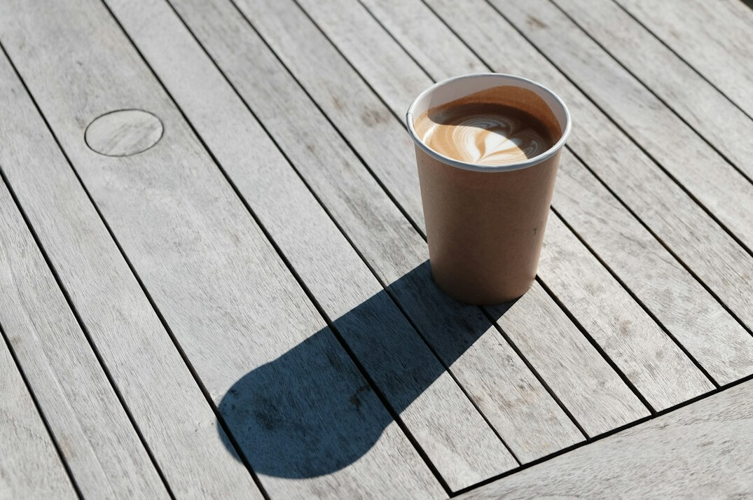 Newspapers and a cup of coffee on a wooden table in daylight